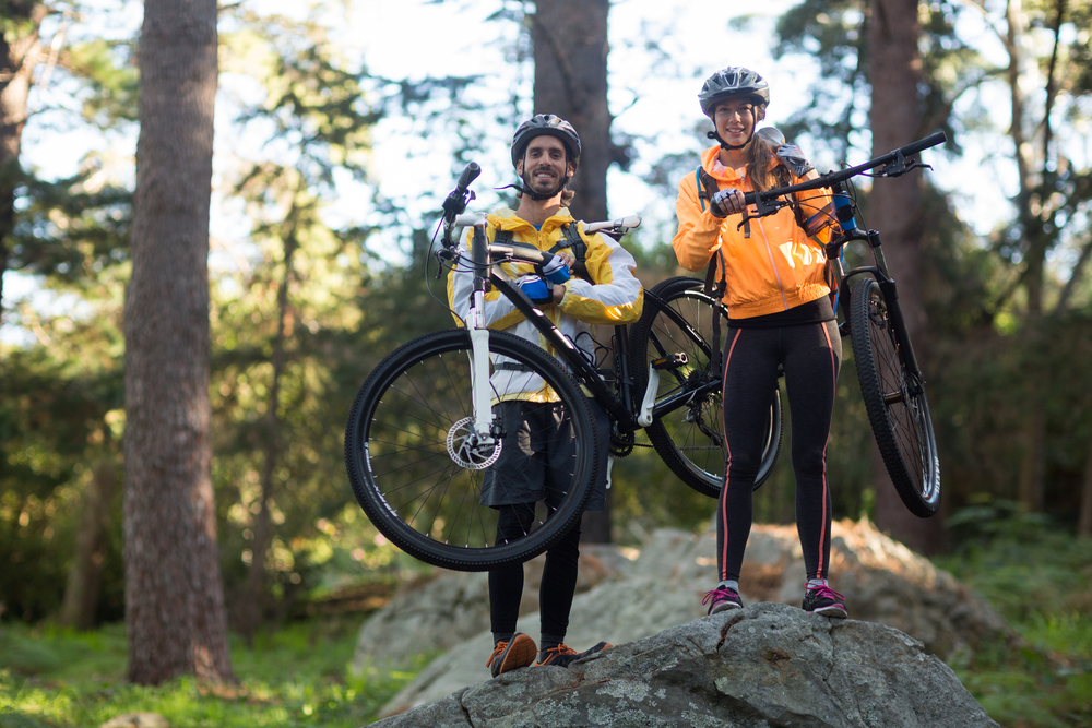 Portrait of biker couple carrrying mountain bike in countryside forest